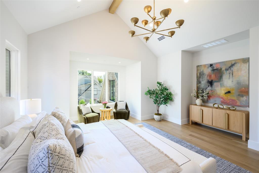 Spacious primary suite with vaulted ceiling and white oak ceiling beams, sitting area and windows overlooking backyard