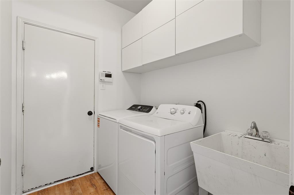 White upper cabinetry, utility sink, and wood-finish flooring