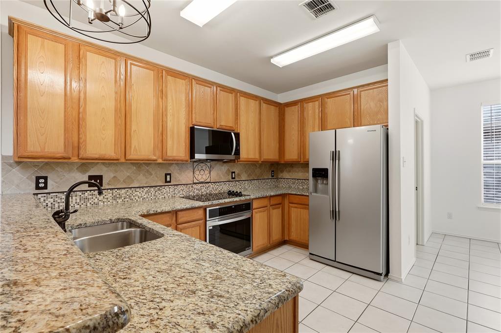 Kitchen featuring granite-style countertops, wood-finish cabinetry, stainless steel appliances, a tile backsplash, and tile flooring