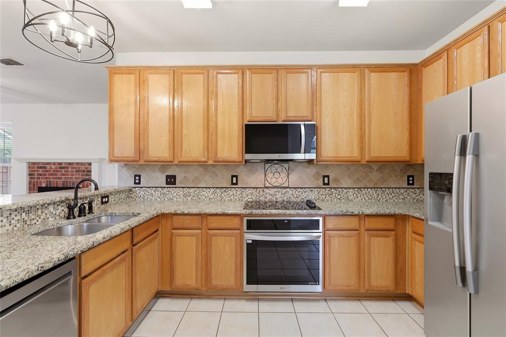 Wood cabinetry with stainless steel appliances, dual basin sink, and tile flooring