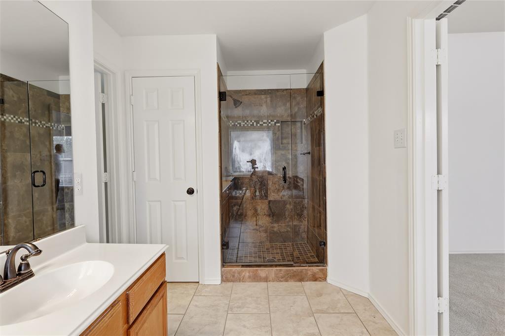 Spacious bathroom featuring a glass-enclosed shower with tiled walls and floor, a single vanity with a white countertop, and tiled flooring