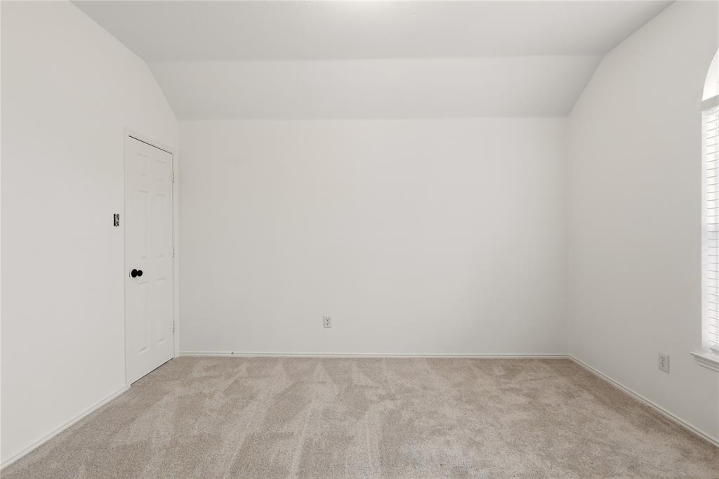 Carpeted flooring, vaulted ceiling, arched window with horizontal blinds, and a paneled door with black hardware