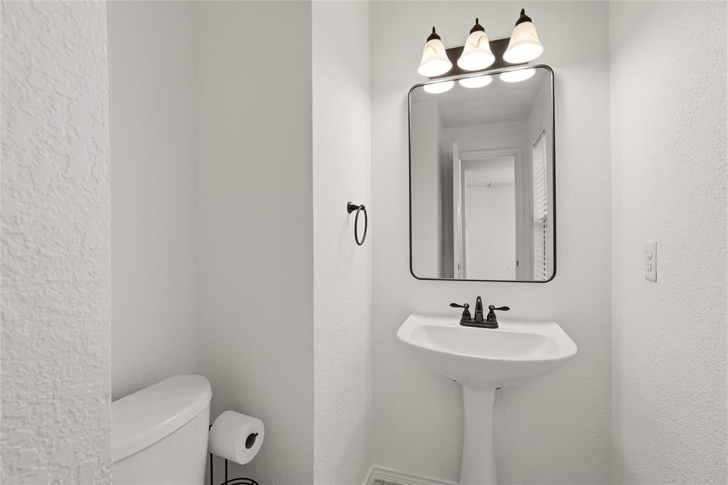 Pedestal sink with dark bronze faucet, framed mirror, and three-light vanity fixture