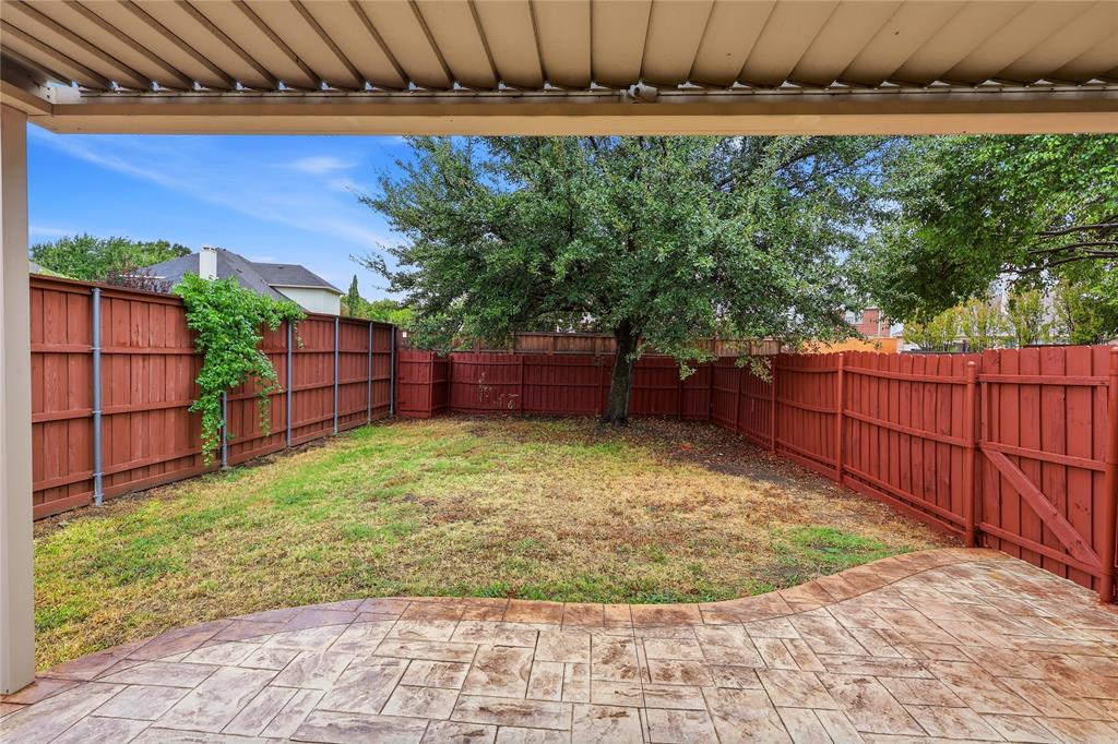 Covered patio with stamped concrete flooring, red-stained privacy fence, and mature tree