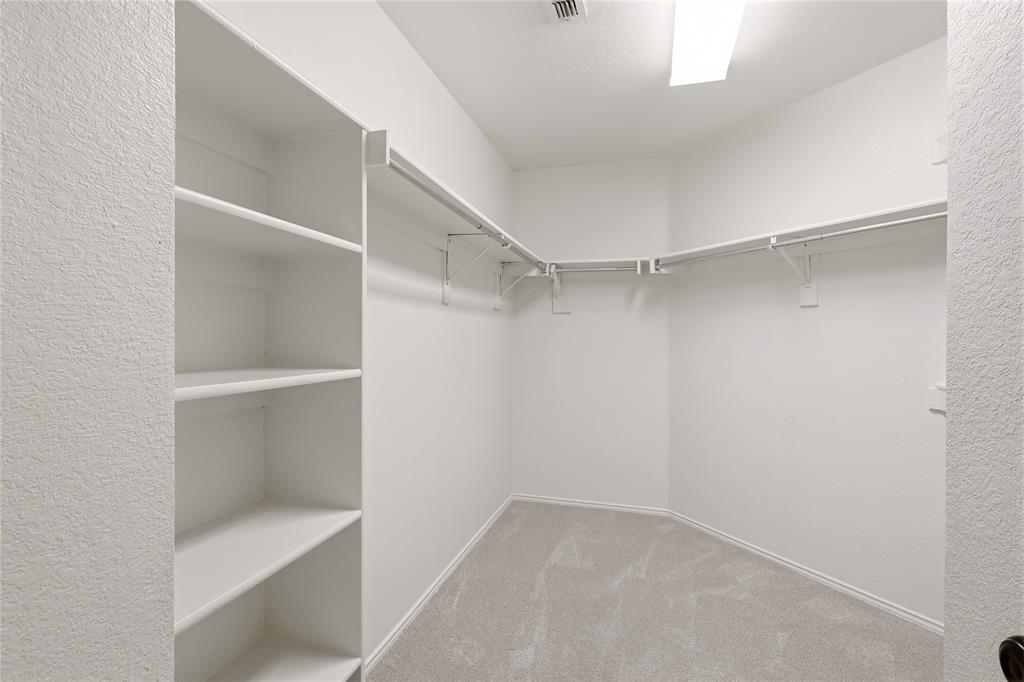 Walk-in closet featuring white shelving, multiple hanging rods, and light-toned carpeting