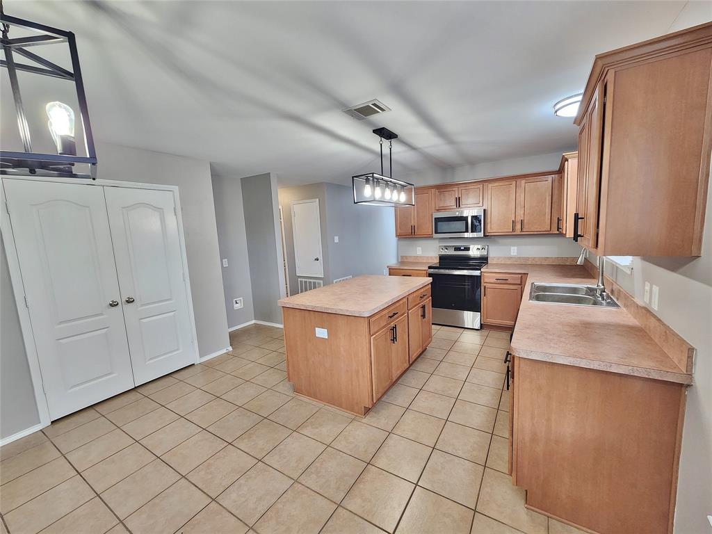 Kitchen featuring a central island, stainless steel appliances, extensive cabinetry, and neutral-toned tile flooring Kitchen featuring a central island, stainless steel appliances, extensive cabinetry, and neutral-toned tile flooring