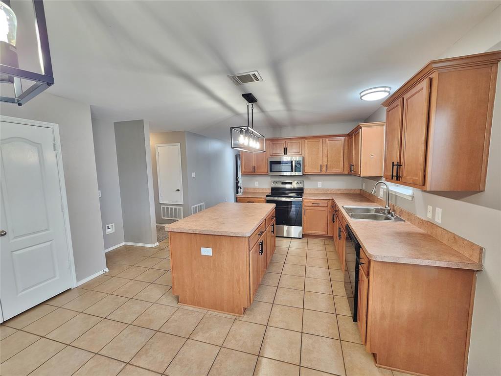 Kitchen featuring an island, integrated stainless steel appliances, wood-finish cabinetry, a double basin sink, and tile flooring Kitchen featuring an island, integrated stainless steel appliances, wood-finish cabinetry, a double basin sink, and tile flooring