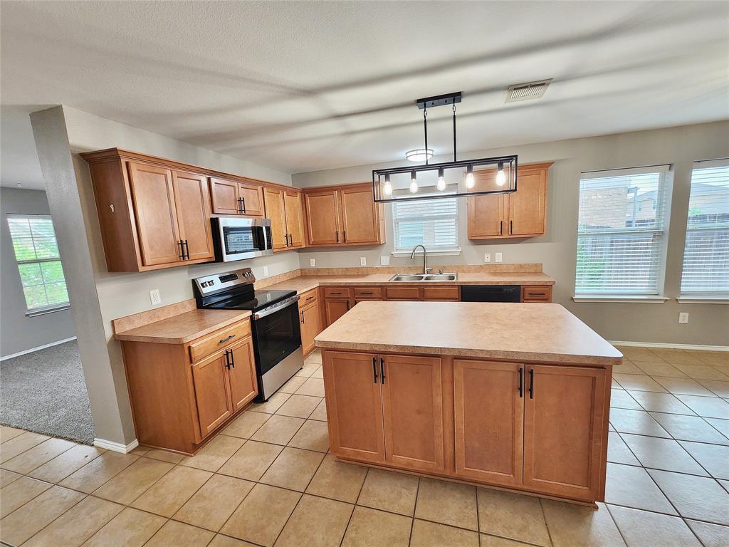 Kitchen featuring tile flooring, wood-finish cabinetry, a central island, stainless steel appliances, and multiple windows Kitchen featuring tile flooring, wood-finish cabinetry, a central island, stainless steel appliances, and multiple windows