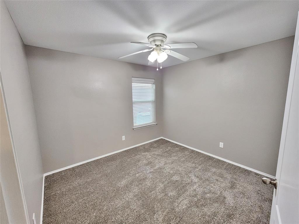Neutral-toned walls, textured carpet flooring, ceiling fan with integrated lighting, and a window with blinds