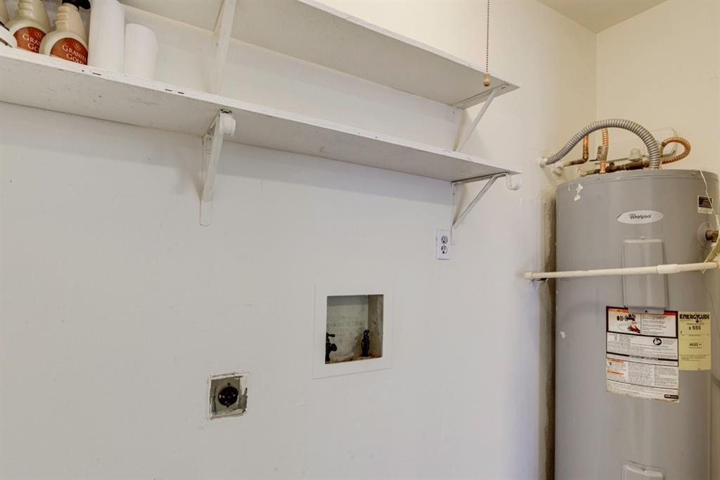 Wall-mounted shelving, recessed laundry hookups, and a dedicated electrical outlet, accompanied by a tank-style water heater