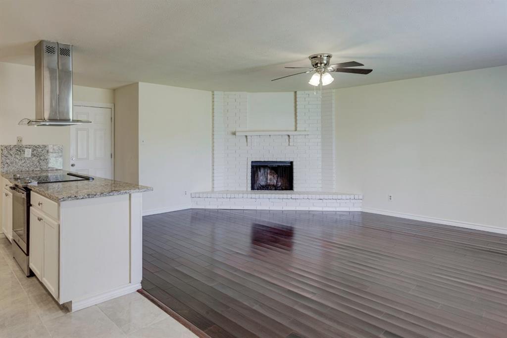 Wood-finish flooring, white painted brick fireplace with raised hearth and mantel, stainless steel chimney-style range hood, granite-topped kitchen island, and ceiling fan Wood-finish flooring, white painted brick fireplace with raised hearth and mantel, stainless steel chimney-style range hood, granite-topped kitchen island, and ceiling fan
