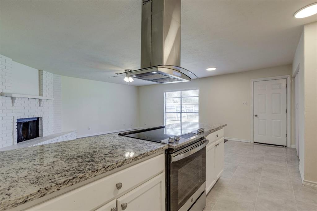 Kitchen featuring a stone-surface island, stainless steel range with overhead chimney vent, white cabinetry, tile flooring, and a painted brick fireplace