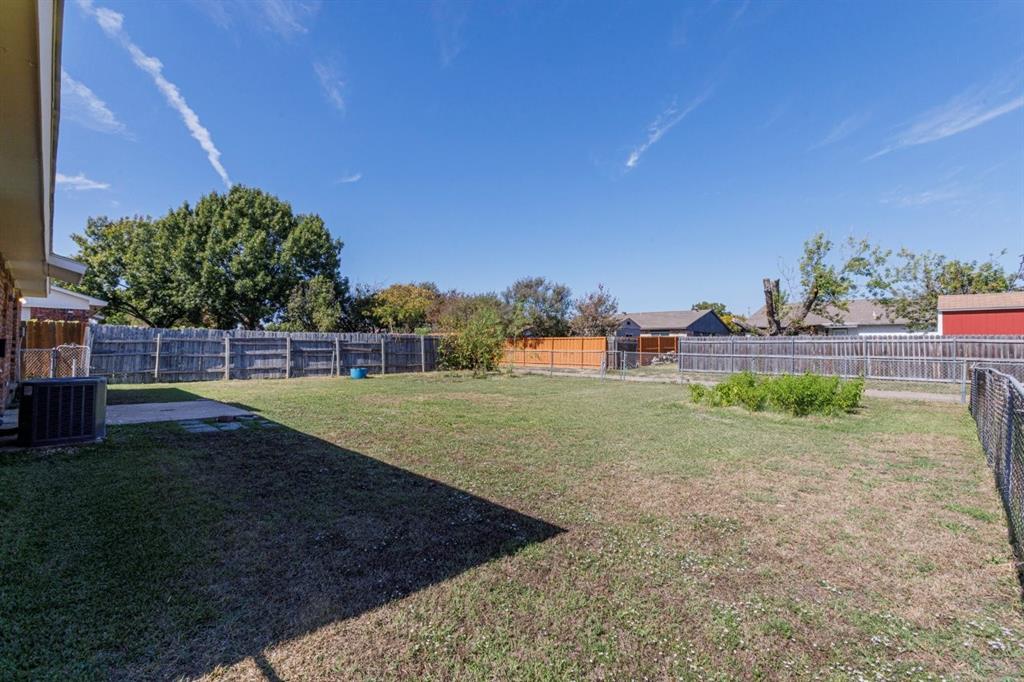 Expansive backyard featuring a concrete patio, perimeter wood fencing, and metal chain-link enclosures
