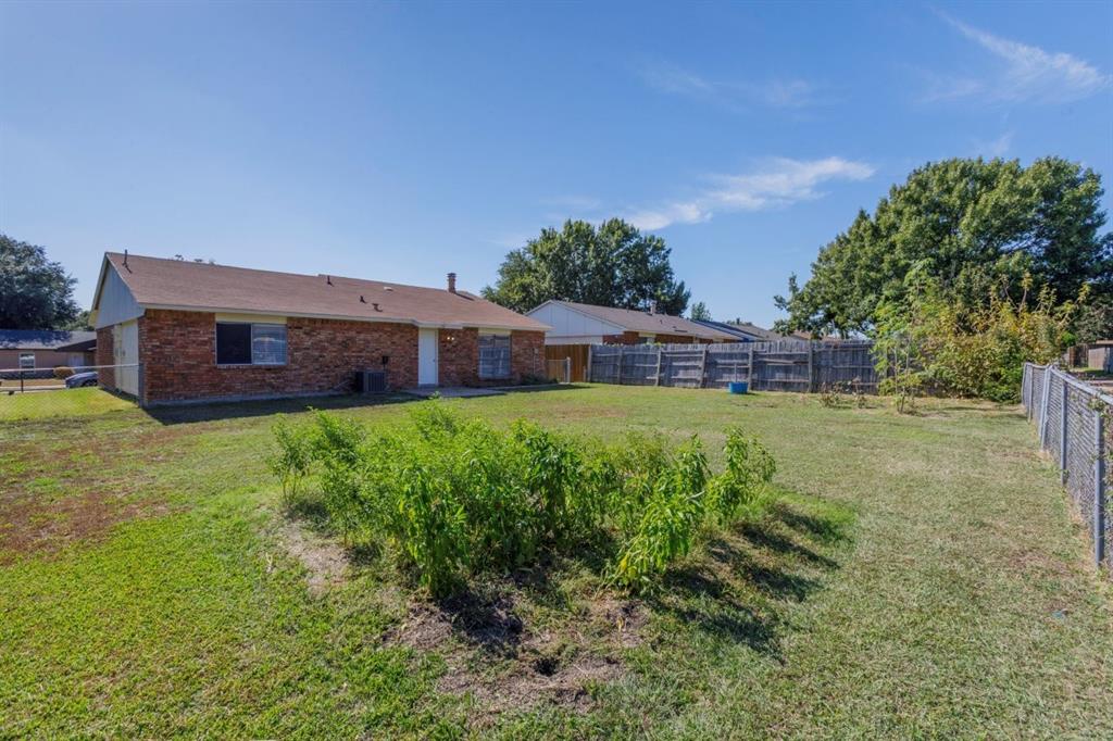 Rear exterior featuring a brick facade, shingle roof, wood privacy fencing, and expansive lawn space