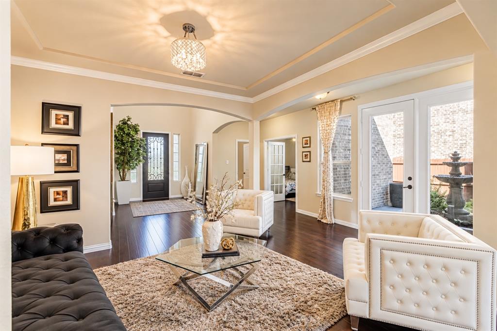 Tray ceiling with a decorative chandelier, wood-finish flooring, and French doors opening to an exterior fountain Tray ceiling with a decorative chandelier, wood-finish flooring, and French doors opening to an exterior fountain