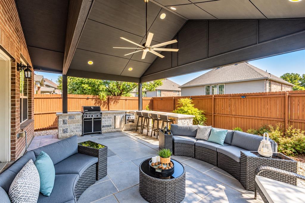 Covered patio with a built-in outdoor kitchen, recessed lighting, ceiling fan, and stone-accented bar