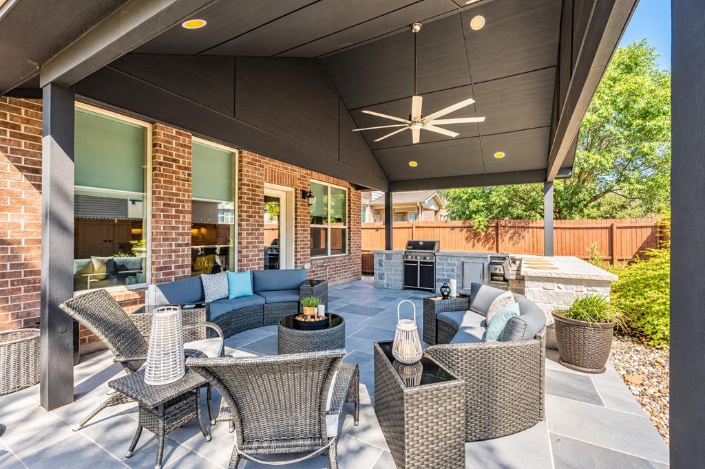 Expansive covered patio featuring a ceiling fan, recessed lighting, stone flooring, and a built-in outdoor kitchen with grill