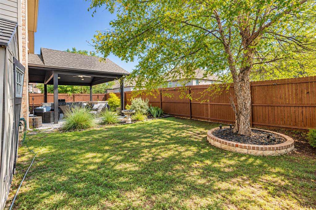 Expansive backyard featuring a manicured lawn, a covered patio with a ceiling fan, and mature trees