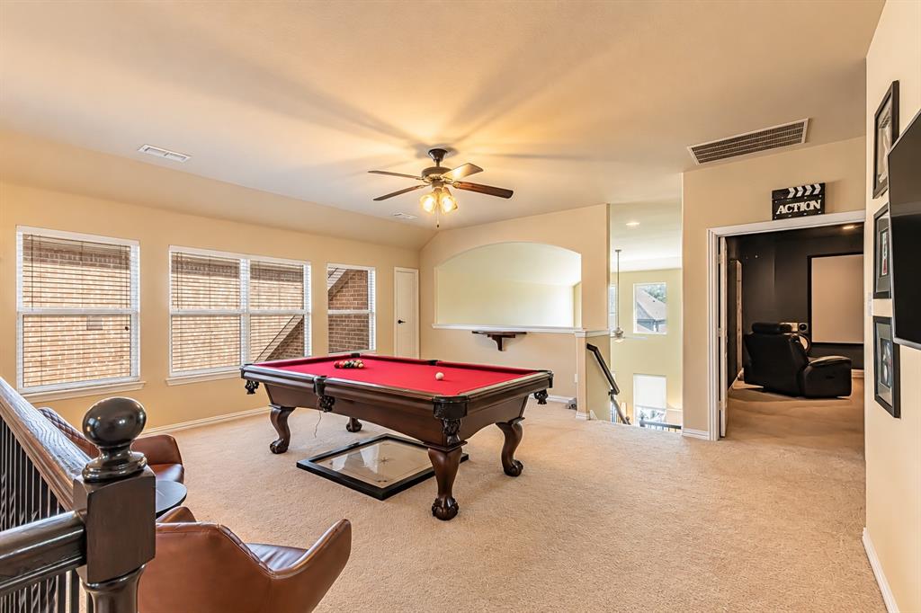 Carpeted recreation area featuring a ceiling fan, multiple windows, and a built-in railing
