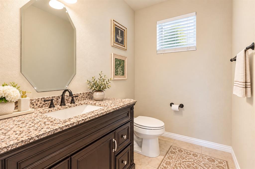 Elegant bathroom featuring a dark wood vanity with dual-sink functionality, granite-look countertop, octagonal framed mirror with integrated lighting, and a spacious layout Elegant bathroom featuring a dark wood vanity with dual-sink functionality, granite-look countertop, octagonal framed mirror with integrated lighting, and a spacious layout