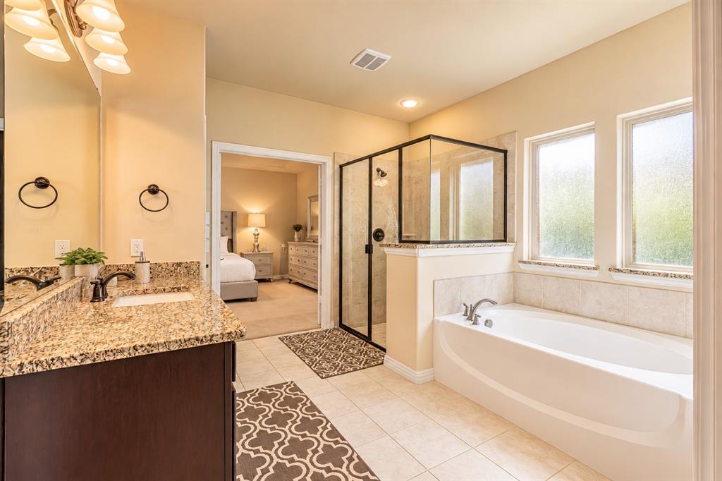 Bathroom featuring a spacious soaking tub, glass-enclosed shower, dual vanity with granite-style countertop, and tile flooring