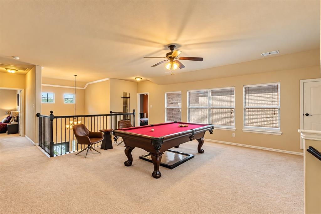 Spacious loft area featuring carpet flooring, multiple windows with blinds, a ceiling fan, and black metal railing overlooking the lower level