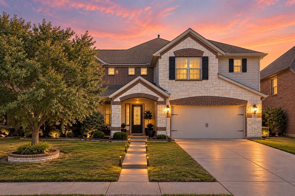 Brick and stone facade with arched entryways, integrated two-car garage, and a manicured lawn with pathway lighting