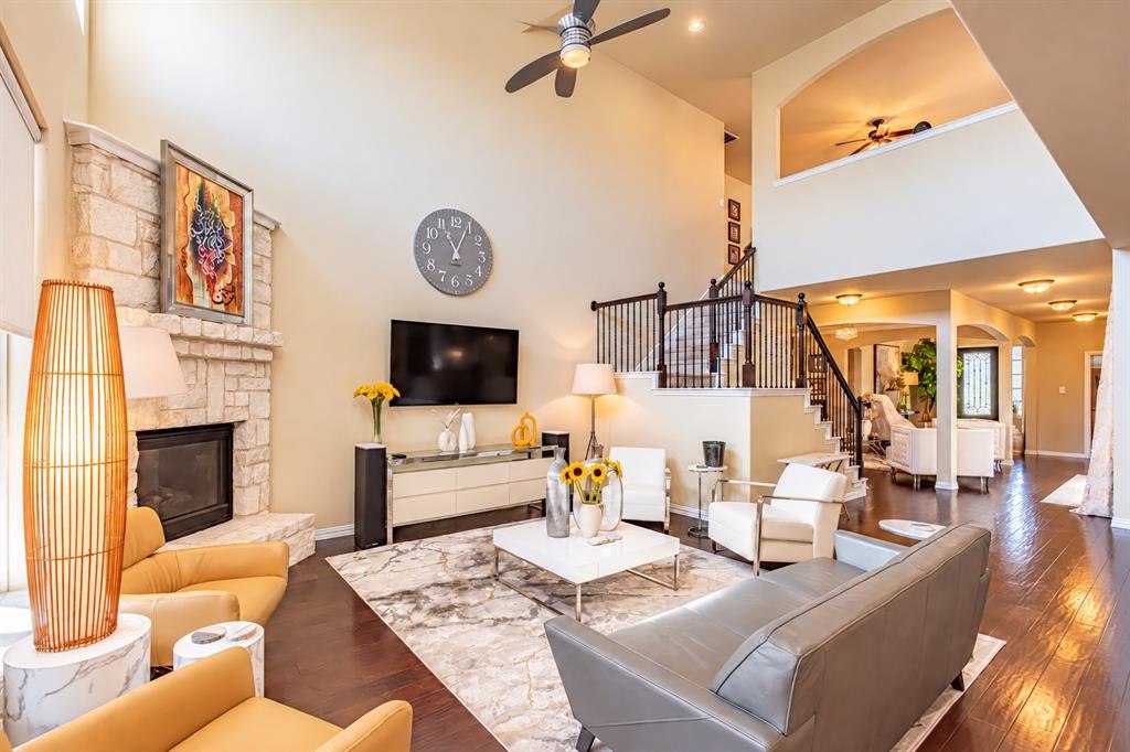 Soaring two-story living room featuring a fireplace with stone surround, recessed lighting, and hardwood flooring