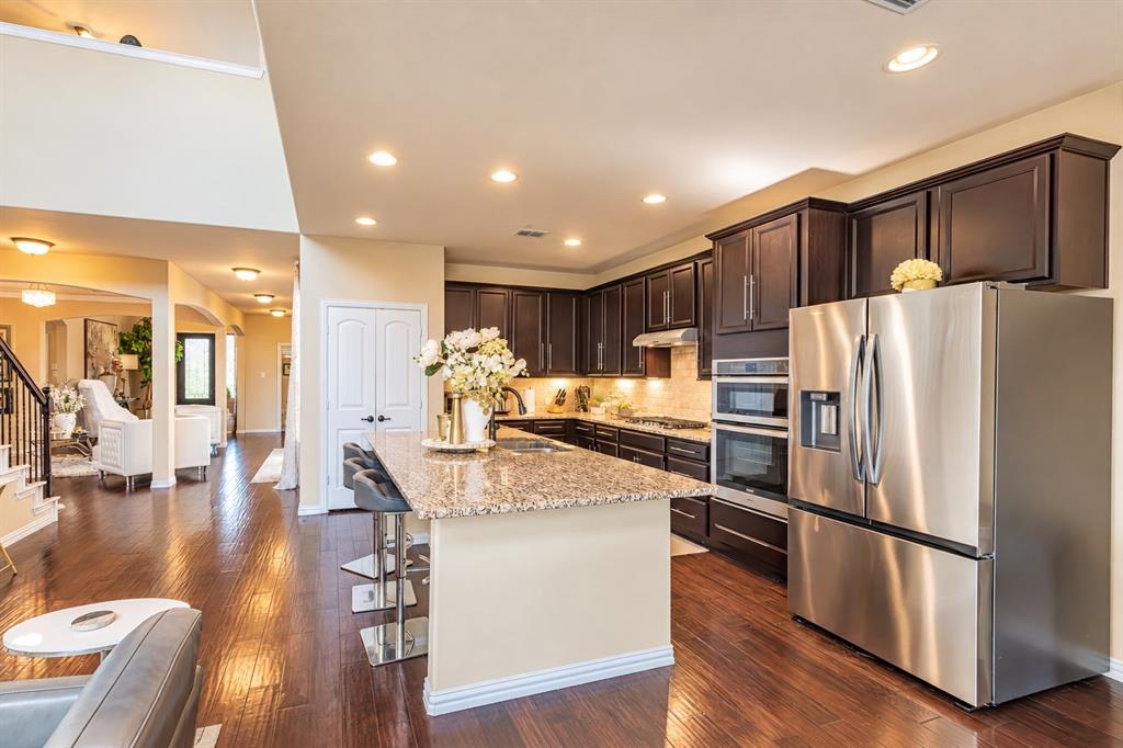 Chef's kitchen featuring dark cabinetry, stainless steel appliances including dual wall ovens, granite countertops, a large center island with seating, recessed lighting, and an open layout connecting to the main living spaces