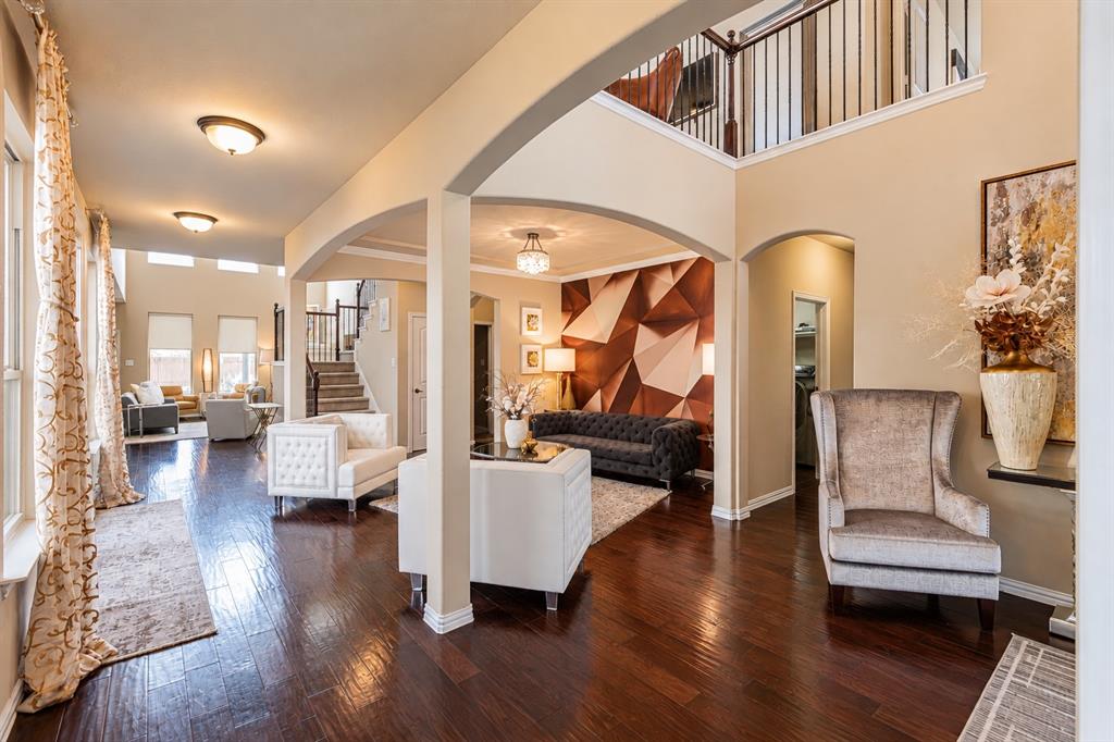 Two-story interior with dark wood-finish flooring, arched doorways, a coffered ceiling, and a second-story landing with black metal railing Two-story interior with dark wood-finish flooring, arched doorways, a coffered ceiling, and a second-story landing with black metal railing