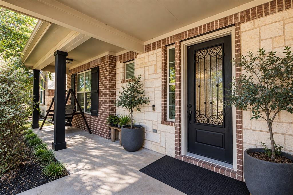 Covered front porch featuring a black decorative glass entry door, brick and stone exterior, and black-painted columns Covered front porch featuring a black decorative glass entry door, brick and stone exterior, and black-painted columns