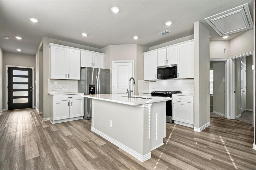 Kitchen featuring an island with a sink, stainless steel appliances, white cabinetry, recessed lighting, and wood-finish flooring