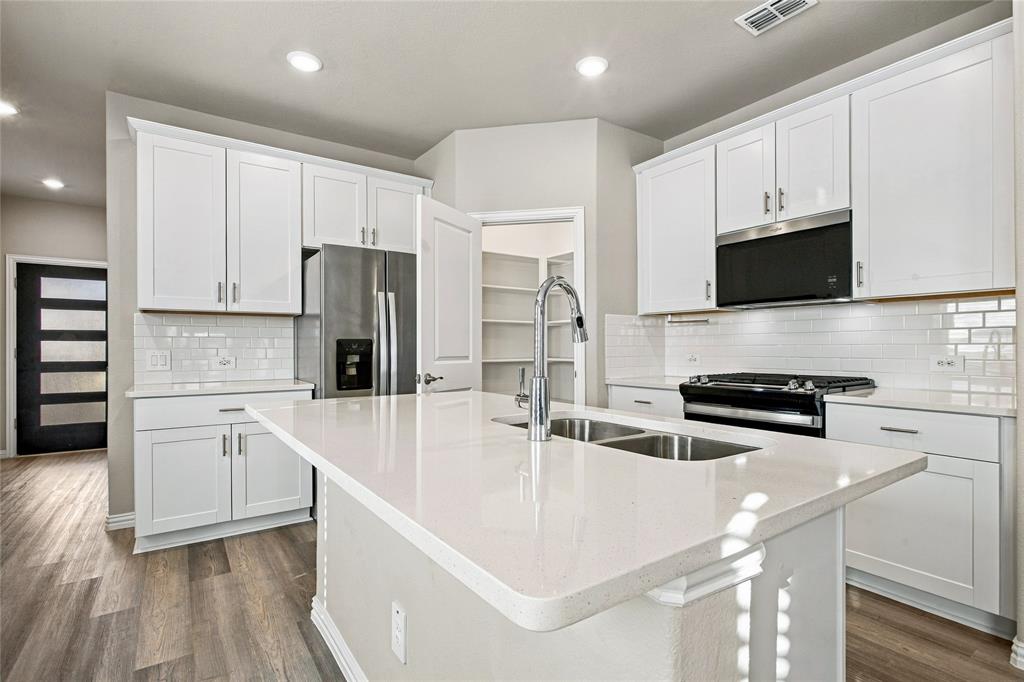 Kitchen featuring white cabinetry, stainless steel appliances, a center island with double sink, and wood-finish flooring