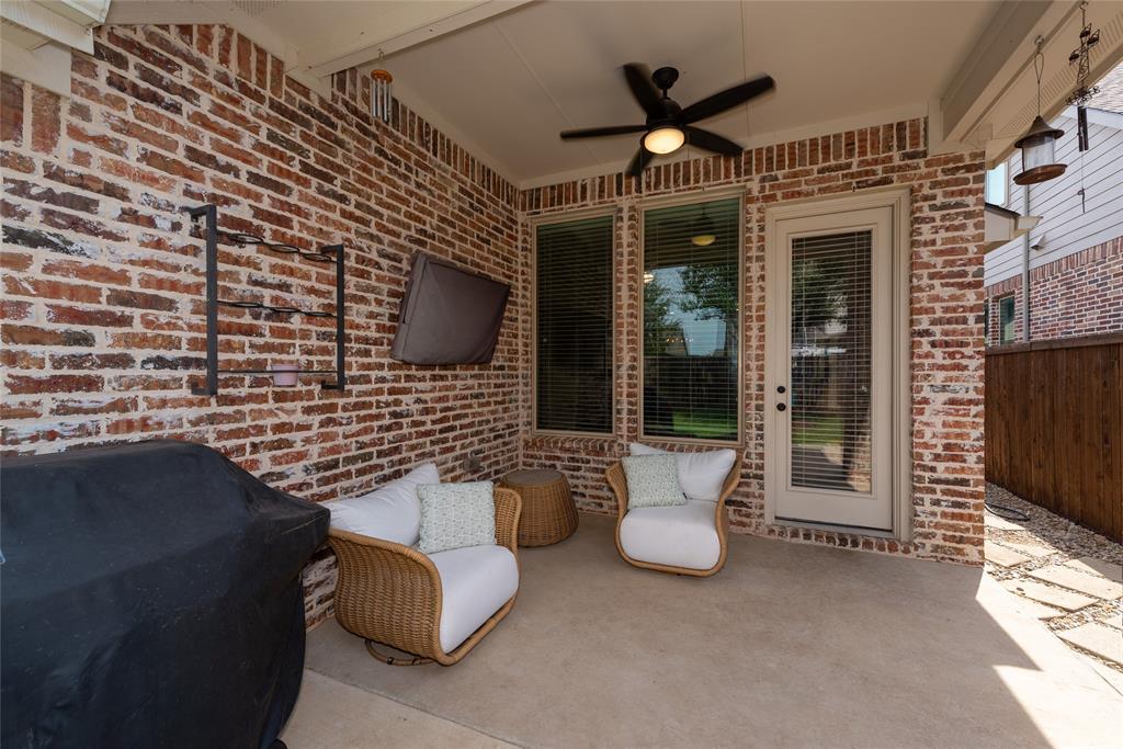 Covered patio featuring a ceiling fan, brick accent wall, and a full-light door with integrated blinds