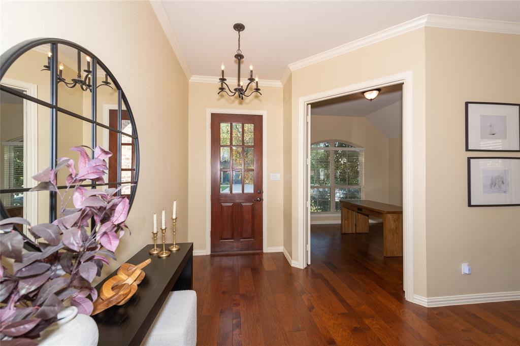 Hardwood flooring, crown molding, a paneled entry door with glass inserts, and a chandelier lighting fixture Hardwood flooring, crown molding, a paneled entry door with glass inserts, and a chandelier lighting fixture