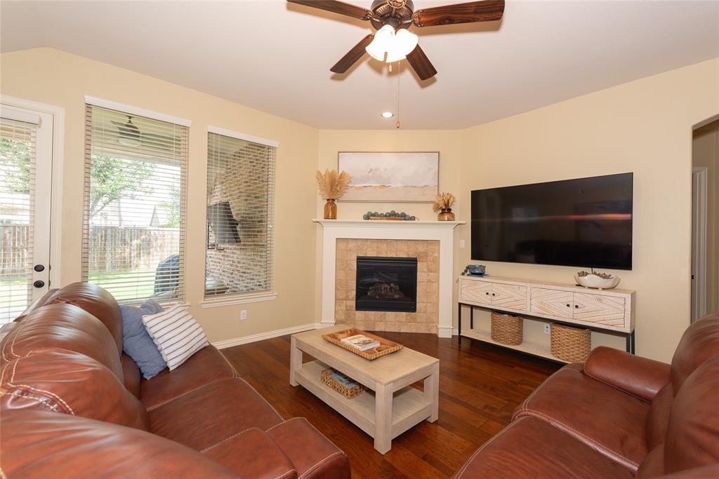 Wood-finish flooring, corner fireplace with tile surround, ceiling fan, and multiple windows Wood-finish flooring, corner fireplace with tile surround, ceiling fan, and multiple windows