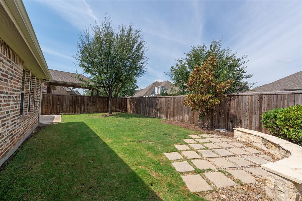 Expansive backyard featuring a manicured lawn, stone paver patio, stone retaining wall, and wood privacy fencing