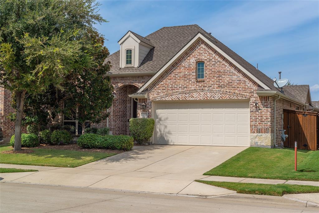 Brick facade with stone accents, dormer window, attached garage, concrete driveway, and manicured landscaping