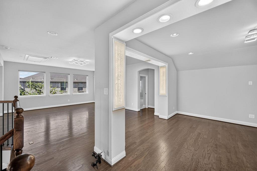 Open interior space featuring wood-finish flooring, architectural cased openings, integrated soffit lighting, and recessed ceiling illumination