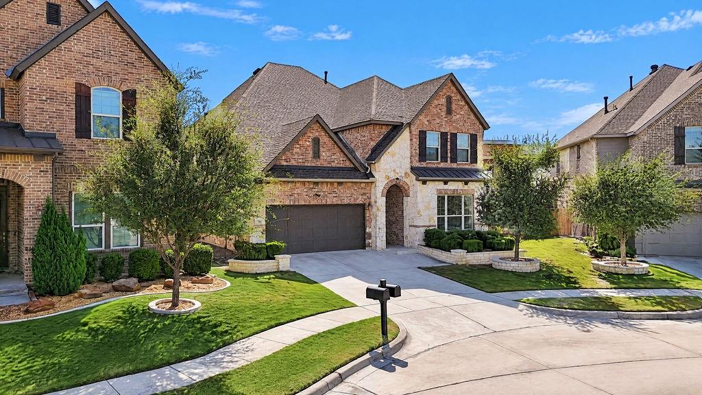 Multi-gable exterior featuring a combination of brick and stone masonry, dark-toned shutters, a multi-car garage, and professional landscaping with circular stone-bordered planter beds Multi-gable exterior featuring a combination of brick and stone masonry, dark-toned shutters, a multi-car garage, and professional landscaping with circular stone-bordered planter beds