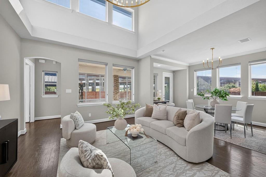 High-ceilinged room featuring wood-finish flooring, large-format windows, and two tiered-arm chandeliers