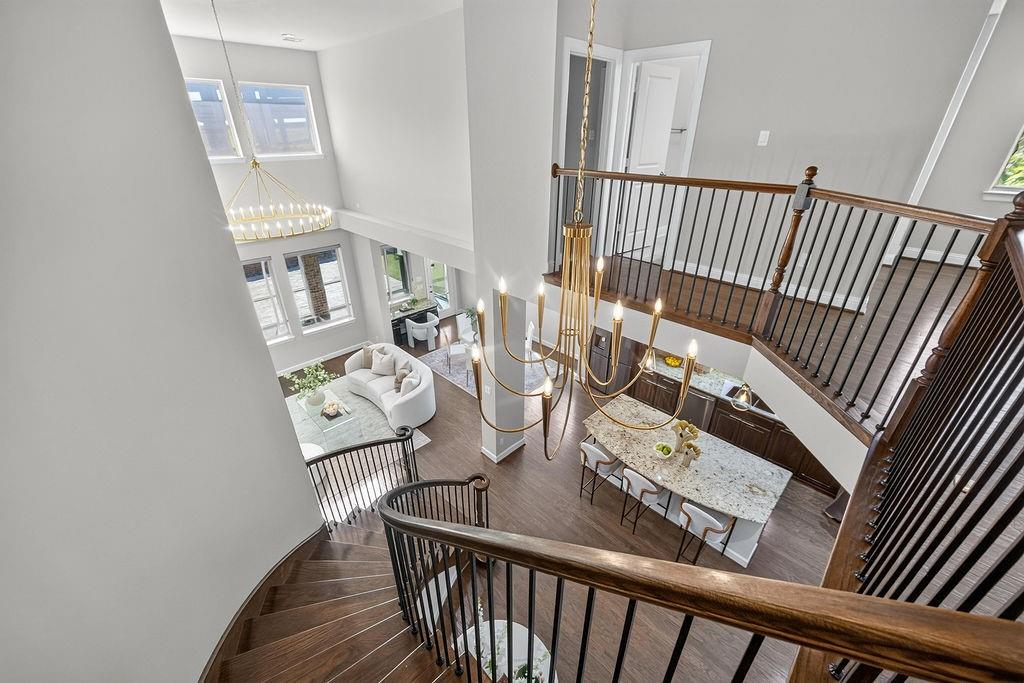 Open floor plan featuring wood-finish flooring, two-story ceilings, a curved staircase with a metal balustrade, a multi-tier chandelier, and a stone-topped kitchen island