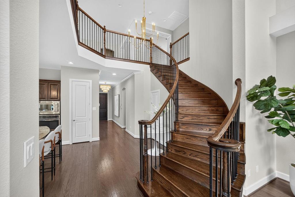 Curved staircase featuring wood-finish treads, a polished wood handrail, and black iron balusters, complemented by a multi-tiered chandelier and wood-finish flooring