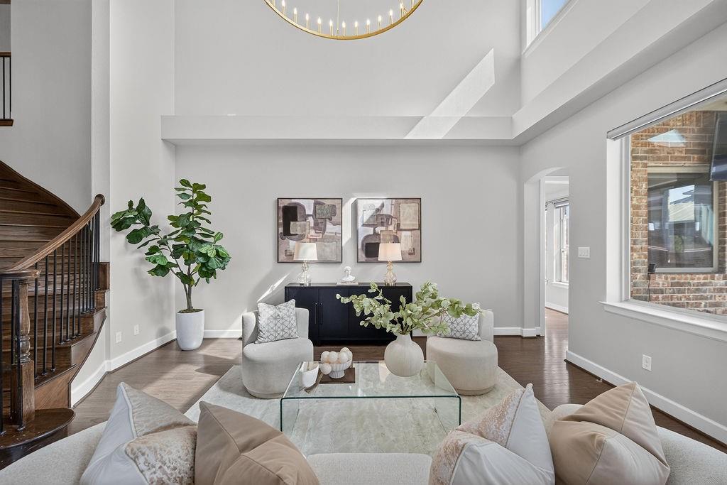 Double-height ceiling, wood-finish flooring, grand circular chandelier, and a curved staircase featuring a dark wood handrail with vertical metal balusters