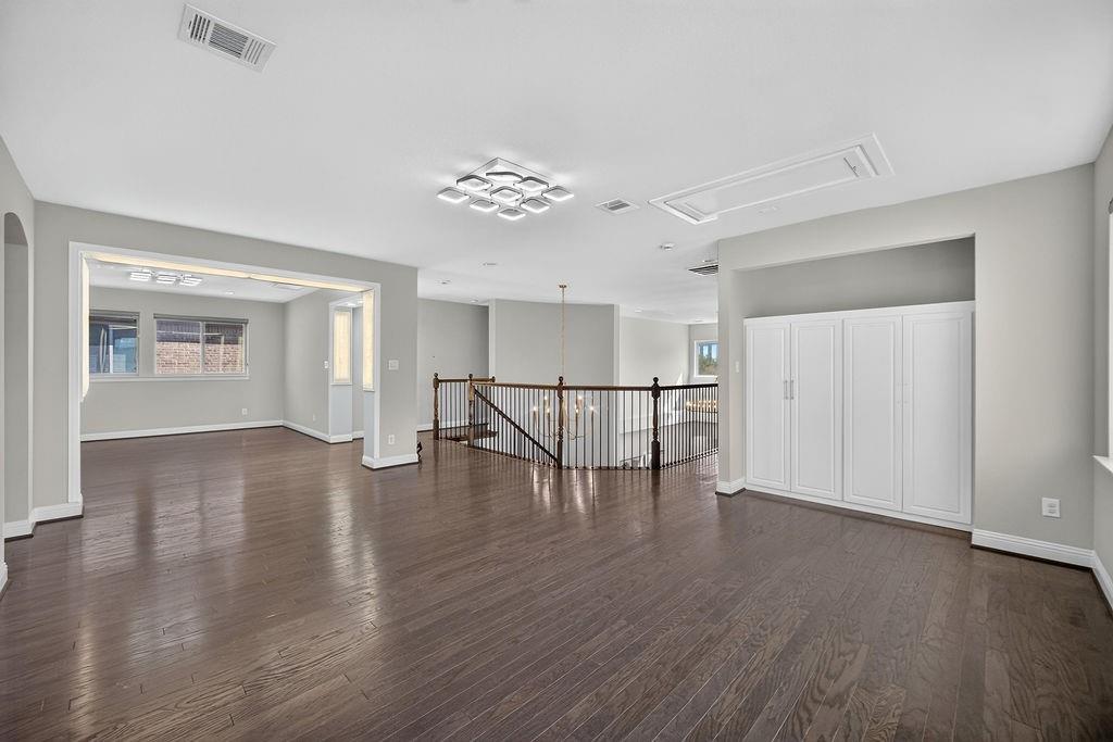 Open-concept area featuring wood-finish flooring, built-in cabinetry, tiered modern ceiling lighting, and a balustrade staircase