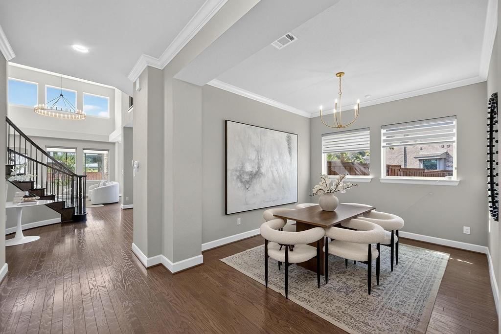 Open-concept interior featuring wood-finish flooring, crown molding, double-height ceilings, metal staircase railing, and tiered chandelier lighting