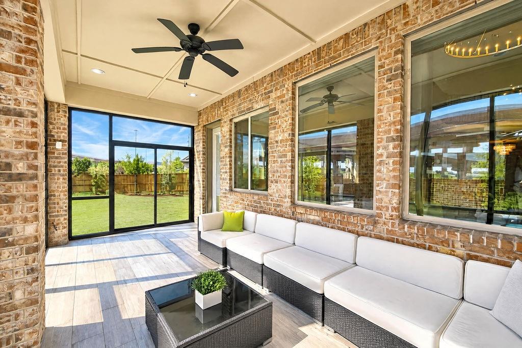 Covered patio featuring brick exterior walls, wood-finish tile flooring, large multi-panel glass sliding doors, recessed ceiling lighting, and a black ceiling fan
