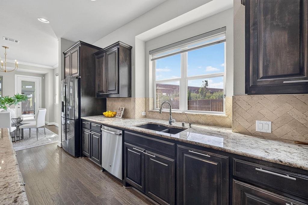 Kitchen featuring dark wood cabinetry, natural stone countertops, herringbone-pattern tile backsplash, stainless steel appliances, and wood-finish flooring