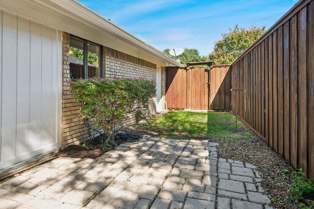 Brick exterior with white vertical siding, established shrubbery, a paved patio, a wood privacy fence and 2nd green space