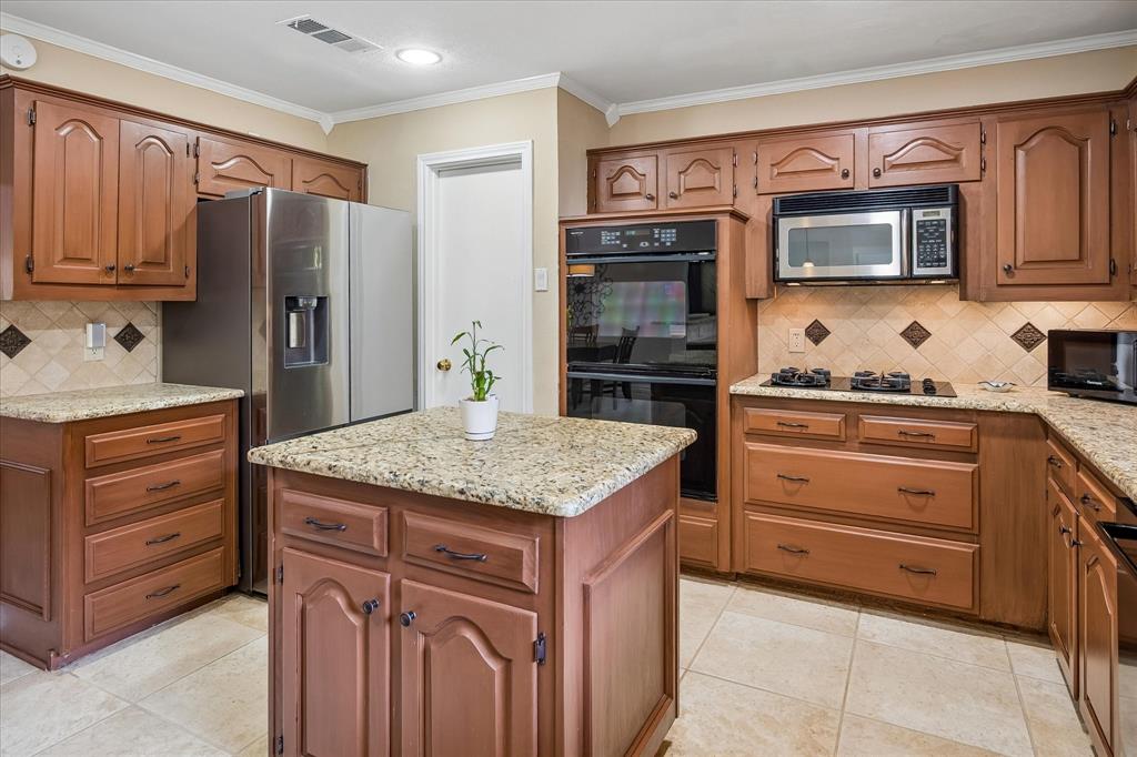 Kitchen featuring wood cabinetry, light-toned granite countertops, a built-in double oven, and a built-in microwave